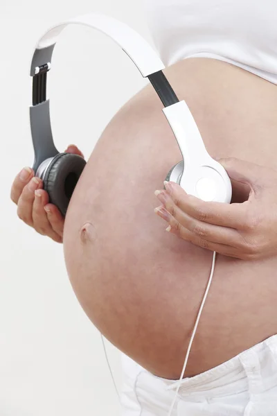 Primer plano de la mujer embarazada sosteniendo los auriculares sobre el vientre —  Fotos de Stock