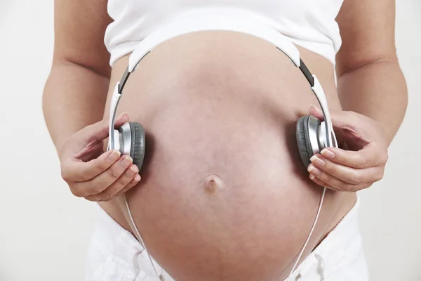 Close Up de mulher grávida segurando fones de ouvido sobre a barriga — Fotografia de Stock