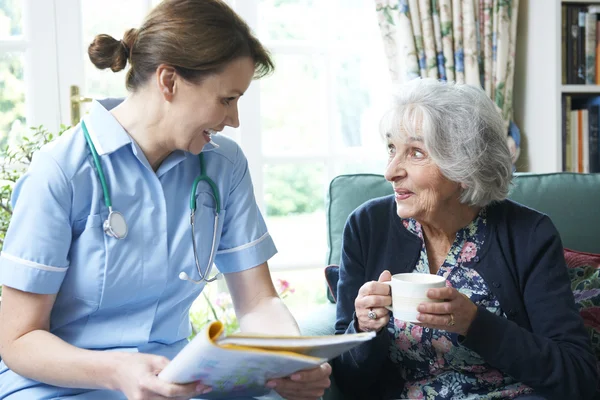 Медсестра обсуждает медицинские записи со старшей женщиной дома — стоковое фото
