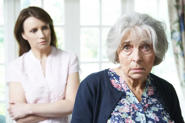 Серьёзная пожилая женщина с обеспокоенной взрослой дочерью дома — стоковое фото