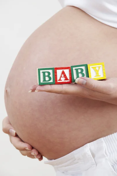 Närbild på gravid kvinna med block stavning baby — Stockfoto