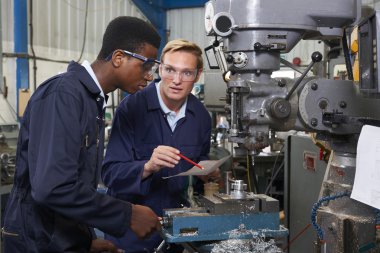 Engineer Showing Apprentice How to Use Drill In Factory clipart