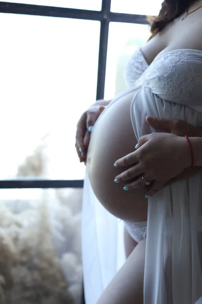 Hamile karnı hamile beyaz elbisesi içinde. Bebek çorapları