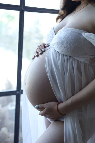 Hamile karnı hamile beyaz elbisesi içinde. Bebek çorapları