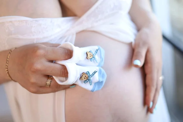 Hamile karnı hamile beyaz elbisesi içinde. Bebek çorapları