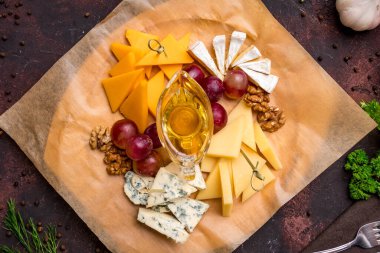 Cheese plate with different cheeses, honey and grapes, italian food on dark table top view