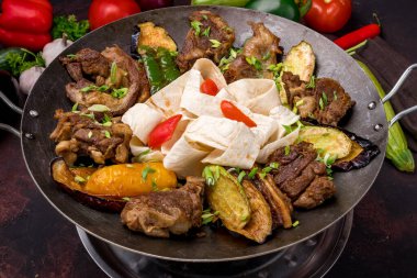 saj of lamb and vegetables on dark table
