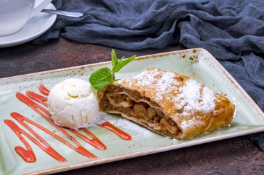 Apple strudel with ice cream on dark table