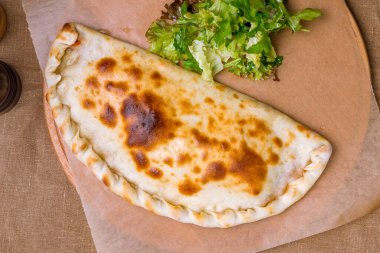 Closed calzone pizza with ham and cheese on the board