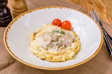 Stroganoff with mashed potatoes on white plate on wooden table