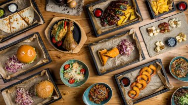 Assorted meat dishes. Burger, fried chicken breast, chicken Salad, potatoes in the country, pork ribs, turkey, wok, cheese plate on a wooden table