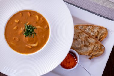 Balık çorbası, beyaz tabakta deniz ürünleri ve kızarmış ekmek.