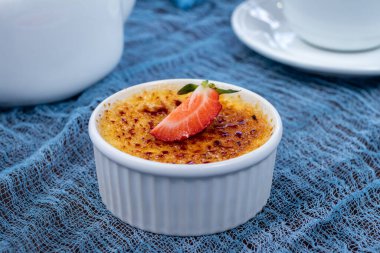 classic dessert creme brulee with strawberry on blue table with tea