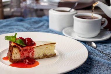 Beyaz tabakta çilekli ve naneli klasik cheesecake.