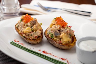 Kömürde kavrulmuş patatesler ve beyaz tabakta ringa balığı.