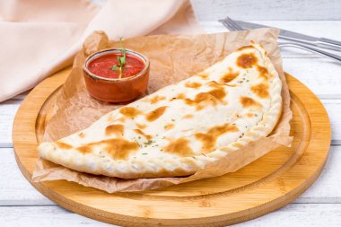 Jambonlu, peynirli ve beyaz ahşap masada domates soslu kapalı calzone pizza.