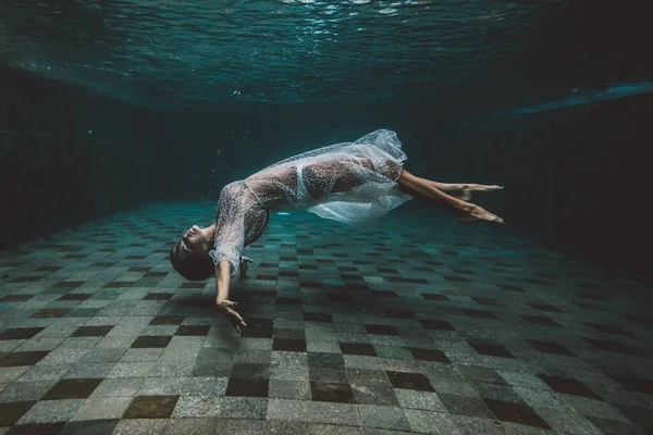 Young dark hair woman in vintage white dress swim underwater Immagini Stock Royalty Free