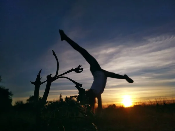 Girl doing split on handstand. A model stands on her hands, doing gymnastic splits against the blue sky. Healthy lifestyle concept. Silhouette on sunset background. Gymnastic in nature