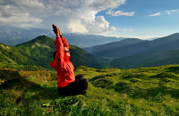Young woman in red jacket sitting in yoga pose in mountains — Stock Photo, Image