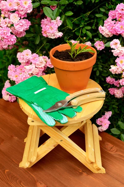 Outils de jardinage sur table en bois et fond de fleurs roses — Photo