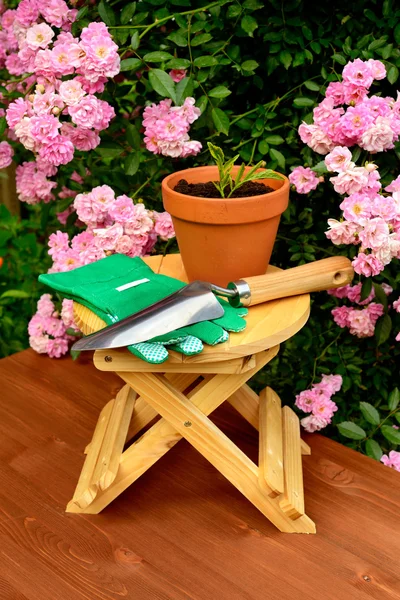 Outils de jardinage sur table en bois et fond de fleurs roses — Photo