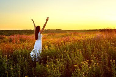 Young woman in white clothes standing in field on sunset