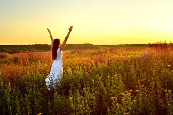 Jovem mulher de roupas brancas em pé no campo ao pôr do sol — Fotografia de Stock