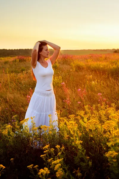 Femeie tânără în haine albe în picioare în câmp pe apus de soare — Fotografie, imagine de stoc