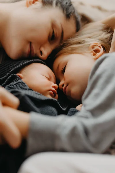 Anne, kızlarının yanında uyumak için uzandı. Anneleriyle sarılıp uyuyan çocukların ev fotoğrafı.