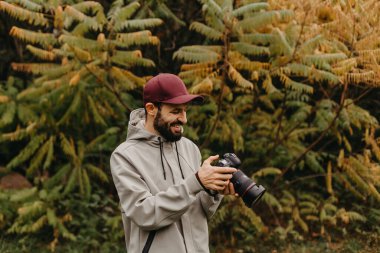 Genç beyaz erkek fotoğrafçı sonbahar parkında fotoğraf çekiyor.