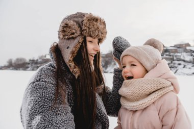 Mutlu anne ve kız çocuğu güneşli kış karı altında eğleniyor, bayram mevsiminde.