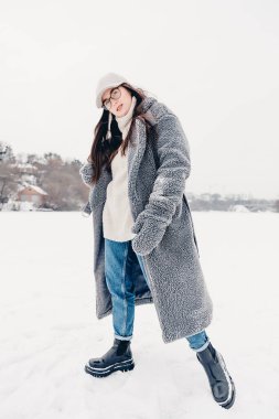 Şık kışlık kıyafetler giymiş çekici bir kızın portresi. Kadın, karla kaplı ve buzlu bir gölde poz veriyor.