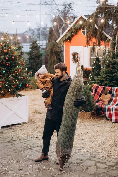 Mutlu aile bir Xmas ağacı alır. Kış tatili ve halk konsepti. Mutlu sakallı baba ve küçük kızı sokak pazarında Noel ağacını seçiyor.