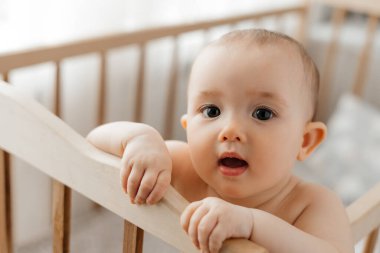 5 aylık bir bebeğin portresi. Parlak bir kreşteki beşikte duruyor. Uyuduktan sonra kameraya bakıp gülümsüyor.