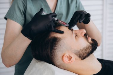 Çekici bir adam klinikte saç dökülmesini tedavi etmek için mezoterapi iğnesi olur. Deriye ve kafa derisine enjeksiyon.
