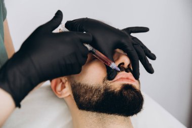 Sakallı şık bir adam estetik kliniğe gidip dudak dolgusu yaptırıyor, yakın plan çekiyor. Çekici Adam, güzellik salonunun arka planında güzellik iğnesi yaptırıyor. Erkekler için yaşlanma karşıtı tedavi