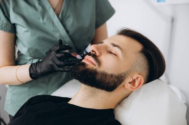 Erkekler için dudak büyüklüğü arttı. Genç, şık sakallı bir kadının dudaklarına hyuleronik asit enjekte edildi.