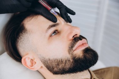 Sakallı şık bir adam estetik kliniğe gidip dudak dolgusu yaptırıyor, yakın plan çekiyor. Çekici Adam, güzellik salonunun arka planında güzellik iğnesi yaptırıyor. Erkekler için yaşlanma karşıtı tedavi