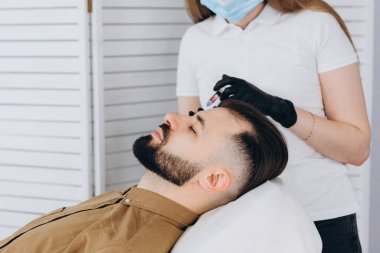 Sakallı şık bir adam estetik kliniğe gidip dudak dolgusu yaptırıyor, yakın plan çekiyor. Çekici Adam, güzellik salonunun arka planında güzellik iğnesi yaptırıyor. Erkekler için yaşlanma karşıtı tedavi