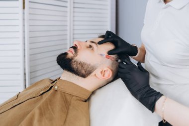 Çekici bir adam klinikte saç dökülmesini tedavi etmek için mezoterapi iğnesi olur. Deriye ve kafa derisine enjeksiyon.