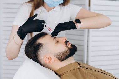 Sakallı şık bir adam estetik kliniğe gidip dudak dolgusu yaptırıyor, yakın plan çekiyor. Çekici Adam, güzellik salonunun arka planında güzellik iğnesi yaptırıyor. Erkekler için yaşlanma karşıtı tedavi