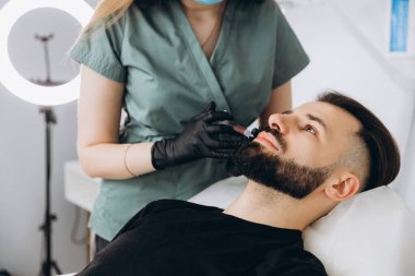 Erkekler için dudak büyüklüğü arttı. Genç, şık sakallı bir kadının dudaklarına hyuleronik asit enjekte edildi.