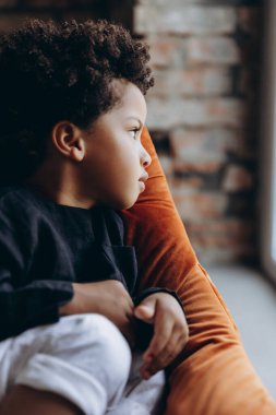 Stüdyoda rahat keten giysiler giymiş koyu tenli bir çocuğun fotoğrafı.