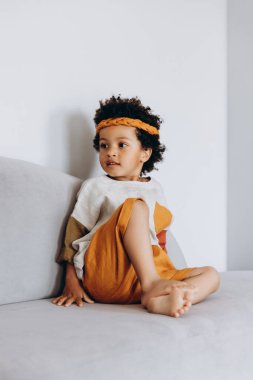 Stüdyoda rahat keten giysiler giymiş koyu tenli bir çocuğun fotoğrafı.