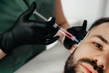 Stylish bearded man visiting aesthetic clinic, getting lips filler, closeup. Man having beauty injection at male spa salon. Anti-aging treatment for men concept