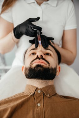 Stylish bearded man visiting aesthetic clinic, getting lips filler, closeup. Man having beauty injection at male spa salon. Anti-aging treatment for men concept