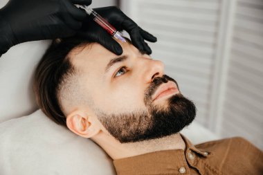 Beauty treatments for a stylish young man with a beard. Beautician makes beauty injections in a man's face