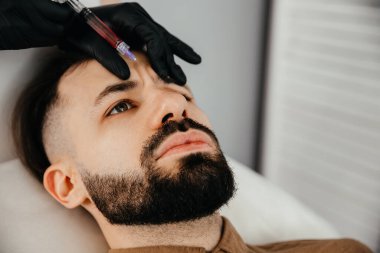 Stylish bearded man visiting aesthetic clinic, getting lips filler, closeup. Man having beauty injection at male spa salon. Anti-aging treatment for men concept