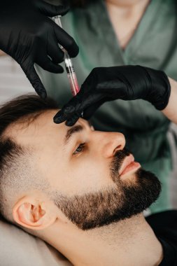 Beauty treatments for a stylish young man with a beard. Beautician makes beauty injections in a man's face