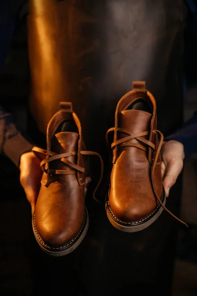 Photo of a pair of quality men\'s leather shoes. Man in apron checking quality of leather details. Manufacturing industry and footwear production concept